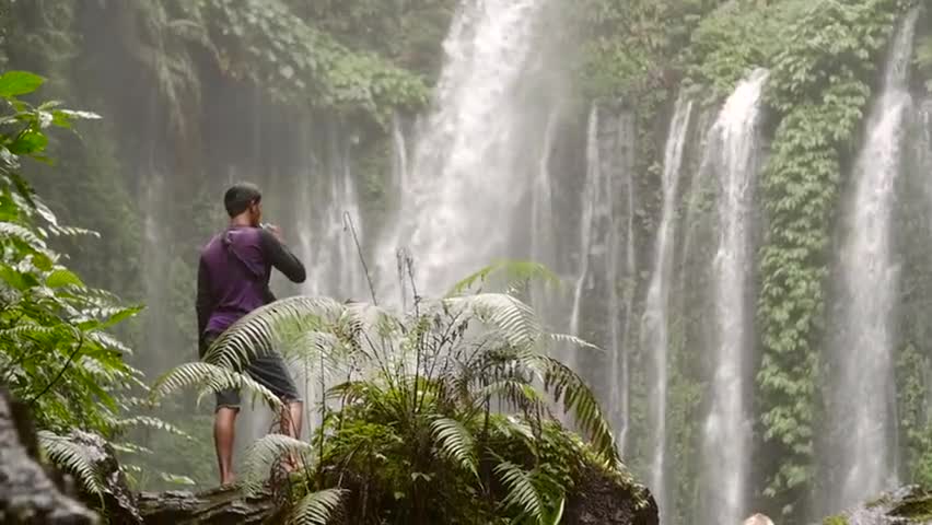Man Vaping in Front of a Large Waterfall